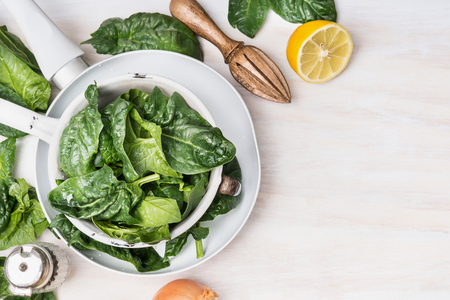 Colander with spinach and vegetarian ingredients on white wooden background, top view, place for text. Clean eating and cooking or diet food conceptの写真素材