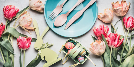 Easter composing with spring tulips , bunny decor, eggs and festive table setting with plate and cutlery, top view, bannerの写真素材
