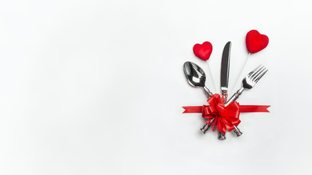 Festive table with red bow, cutlery and two hearts on white background, banner. Layout for Valentines day dinner invitation or menu, banquet, celebration, event