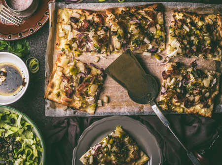 Vegetables tart with leek, served with green salad and dressing on rustic kitchen table background, top view. Tarte flambee - rustic french pie. Vegetarian foodの写真素材