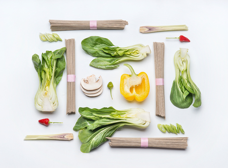 Asian food creative layout on white desk background, top view. Asian cuisine ingredients with soba noodles, vegetables, spices and pak choi. Vegetarian eating and healthy nutrition conceptの写真素材