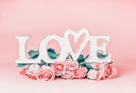 Word LOVE on pastel pink background with roses bunch, front view. Creative female holidays layout with copy space for greetingの写真素材