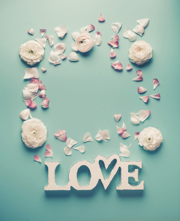 Frame of white word LOVE with pale roses and petals on turquoise blue background, top view. Modern minimal flat lay conceptの写真素材