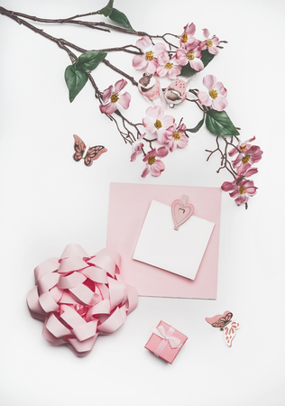Lovely pastel pink greeting card mock up with blossom decoration, hearts, little gift box and bow on white desk background, top view, flat lay. Wedding invitation  layout or Mother Day  conceptの写真素材