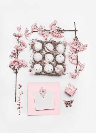 Beautiful pastel pink Easter layout with blossom decoration, hearts, eggs in carton box and greeting card mock up on white desk background, top view, flat lay.の写真素材