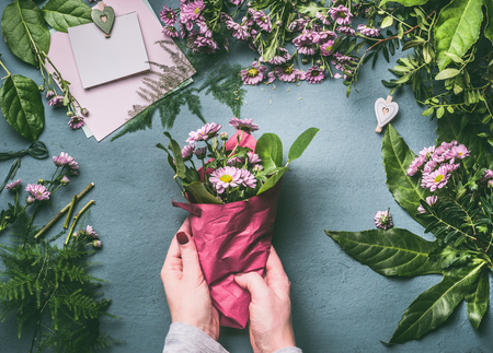 Female hand making beautiful bouquet of pink flowers on florist workspace, top view. Woman wrap bouquet in wrapping paper, step by stepの写真素材