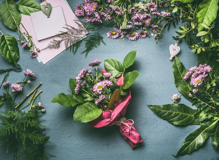 Desk table with bouquet of flowers wrapped in red wrapping paper. Florist workspace with various flowers , decoration  and greeting card mock up , top view, flat layの写真素材