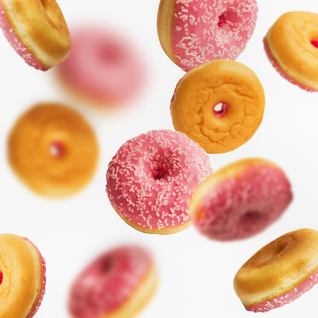 Falling or flying pink glazed donuts with sprinkles on white background, creative layout or patternの写真素材