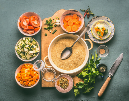 Couscous and vegetarian cooking ingredients in bowls on cutting board with spoon , gray background, top viewの写真素材