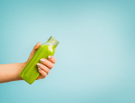 Female hand holding bottle with green summer beverage: smoothie or juice at blue background.の写真素材