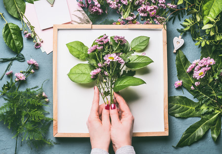 Florist work space . Female hands holding  bunch with green branches and pink flowers, top viewの写真素材