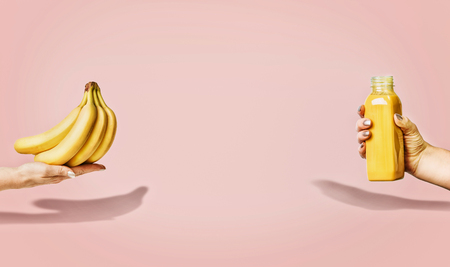 Summer food and beverages background with bananas and yellow drink bottle in female hand at pastel pink background, front view, banner or template.の写真素材