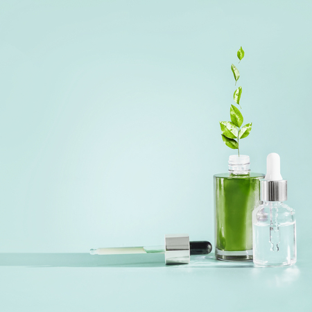 Herbal facial skin care cosmetics bottle with dropper and pipette at blue background . Natural  serum or oil products with green medicinal herb and leaves, front view . Branding mock-upの写真素材
