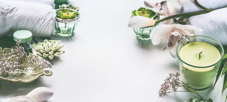 Green spa or wellness background with towels, candle, orchid flowers and body and face care tools...