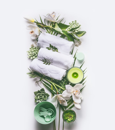 Green spa or wellness composing with towels, candle, tropical leaves , orchid flowers, succulents and body and face care tools and accessories on white background, top viewの写真素材