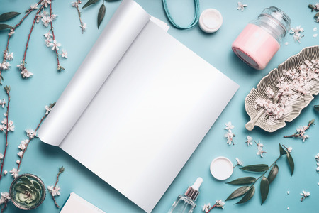 Mock-up of open magazine or catalog for beauty and cosmetic products on pastel blue desktop with twigs and cherry blossom. Modern spring skin care concept, top view, flat lay