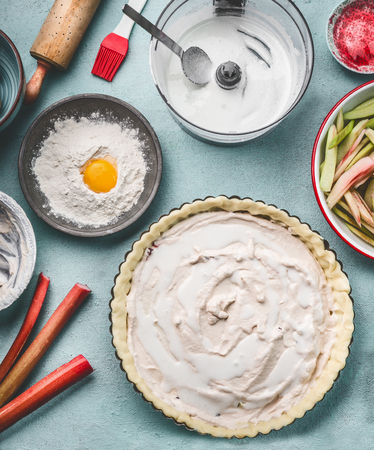 Rhubarb cake preparation. Tart baking pan with pie dough and cream fresh on kitchen table background...