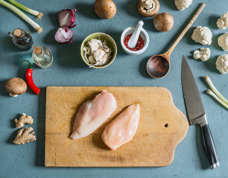 Two chicken breast on cutting board with knife on kitchen table background with ingredients , top view. Cooking preparationの写真素材