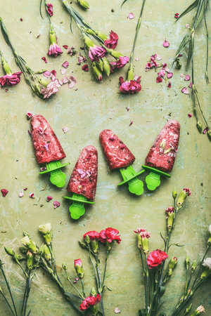 Red homemade fruits and berries ice cream  on teal rustic green table background, decorated with garden flowers, top view.  Country style summer food conceptの写真素材