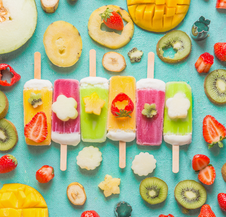 Colorful various  Ice cream popsicles with fresh sliced fruits and berries ingredients on light blue background, top view, flat lay. Frozen tropical juices. Homemade ice cream with exotic fruitsの写真素材