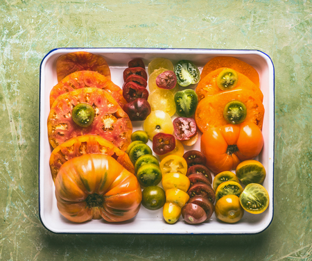 Colorful sliced tomatoes grown in the garden on white tray, top view. The concept of natural...