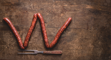 Beef sausages for grill or bbq with meet fork on rustic wooden background, top view. Place for your design, text or recipes. Letter W make with sausagesの写真素材