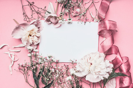 Flowers and petal arrangement around blank paper on pink background with ribbons, top view. Love...