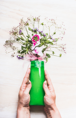 Female hands holding green cosmetic product bottle on white background with plants and flowers , top view. Natural cosmetic conceptの写真素材