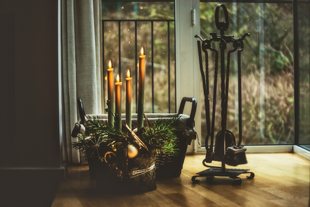 Atmospheric Christmas time at home. Advent wreath with burning candles at window in dark room with fire irons. Winter decor interior with warm lightの写真素材