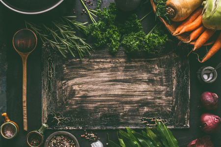 Dark rustic food background frame with vegetarian ingredients: root vegetables, red onion, spices, cooking spoon and seasoning, top view. Clean food. Paleo diet. Healthy eating concept. Copy spaceの写真素材