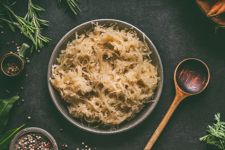 Pickled cabbage in bowl with wooden spoon and seasoning on dark rustic kitchen table background, top view. Vegetarian clean food. Paleo diet. Healthy eating conceptの写真素材