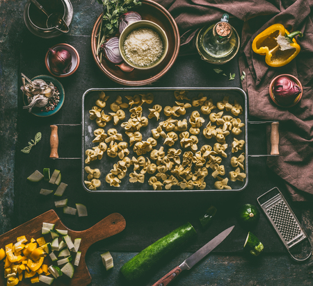 Fresh homemade vegetarian tortellini in tray on dark rustic table background with vegetables ingredients and vintage  kitchen utensils, top view. Home cuisineの写真素材