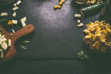 Food and cooking background with homemade vegetarian tortellini on dark rustic table with vegetables ingredients and vintage  kitchen utensils, top view. Home cuisine.の写真素材