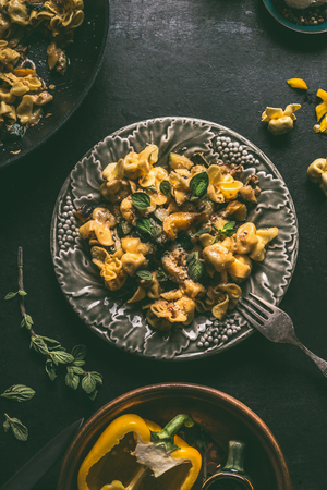 Tasty vegetarian tortellini with creamy vegetables sauce in plate with fork on dark rustic table background with vegetables ingredients and vintage  kitchen utensils, top view. Home cuisineの写真素材