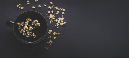 Mug of chamomile tea on dark background, top view with copy space for your design. Healthy tea ingredients and  home remedy for cosmetic treatment. Herbal medicine concept. Template or banner.の写真素材