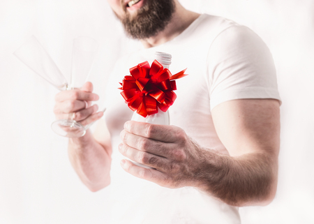 Young man with bottle of champagne and red bow at whiteの写真素材