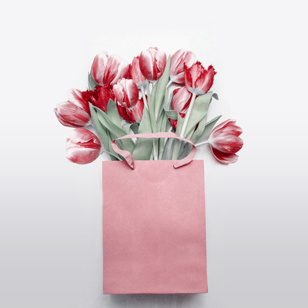 Red tulips bouquet in paper shopping bag on  light gray background. Festive spring flowers bunch. Floral gift composing. Springtime holiday , greeting or sale concept. Copy space for your designの写真素材