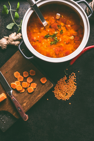 Cooking pot with tasty lentil soup and ladle on dark rustic kitchen table background with ingredients, top view with copy space. Healthy vegan food conceptの写真素材