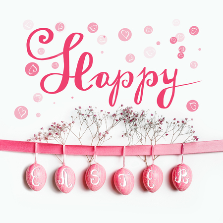 Happy Easter greeting card lettering with hanging pastel pink Easter eggs on ribbon with flowers at white wall backgroundの写真素材