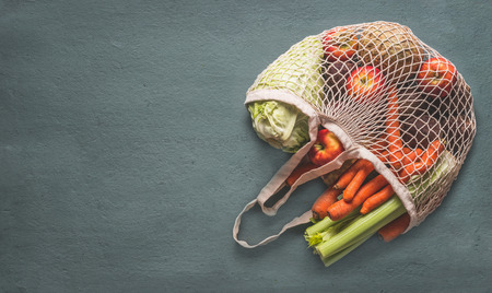 Various farm organic vegetables from local market in net string shopping bag on rustic background, top view with copy space for your design, banner. Clean and healthy food concept. Seasonal vegetableの写真素材