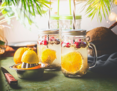 Detox chia seeds drink with orange fruit slice , lemon juice and cranberries in glass jars with drinking straw on kitchen table with ingredients. Summer drinks concept. Fitness and diet nutritionの写真素材