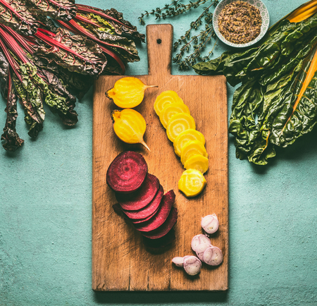 Colorful sliced beetroots with greens ingredients on kitchen table with cutting board, top view. Healthy vegetarian eating and cookingの写真素材