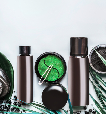 Facial cosmetic products set in black and brown packaging. Modern skin care with eye patch and charcoal powder on light background, top view with copy space. Beauty concept. Branding mock upの写真素材