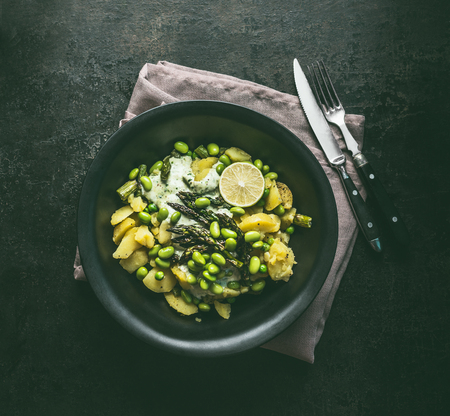 Bowl with potatoes salad with roasted green asparagus, edamame soybeans, lime and green peas on dark rustic kitchen table background, top view. Copy space. Healthy vegetarian food.の写真素材