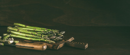 Green asparagus on wooden cutting board with knife on dark rustic kitchen table background . Copy spaceの写真素材