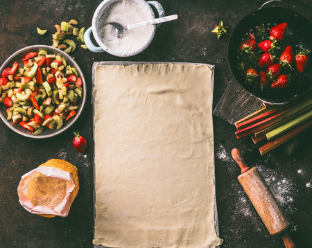 Sheet of pastry dough on rustic kitchen table with rhubarb and strawberries ingredients for strudel pie, top view. Seasonal baking. Organic food. Step by stepの写真素材