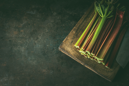 Close up of rhubarb stems on wooden cutting board on dark rustic background. Seasonal organic food . Copy spaceの写真素材