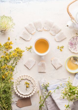 Cup with frame of tea bags of herbal tea on white table background, top view. Herbal tea setting with teapot , honey and fresh medical herbs and flowers. Copy space. Healthy preventive drink treatmentの写真素材
