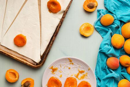 Croissants baking preparation with dough and apricots on light mint table background, top viewの写真素材