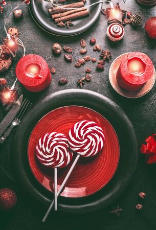 Christmas candy lollipops on red festive table setting with burning candles, fairy lights ,  cinnamon, nuts and holiday decoration. Top viewの写真素材